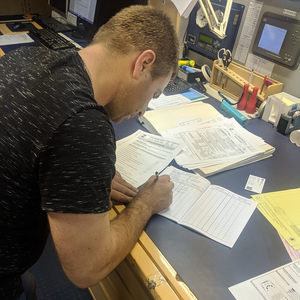 A crew member manually calculating and writing up a noon report by hand
